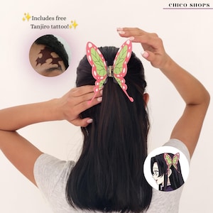 May include: A butterfly-shaped hair claw clip featuring a green and pink geometric pattern. The clip is secured in dark hair. Text on the image includes "CHICO SHOPS" and "Includes free Tanjiro tattoo!" along with an inset showing a forehead tattoo.