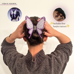 May include: A purple and white butterfly-shaped hair claw clip with a translucent wing pattern. The clip is shown in hair, accompanied by a circular inset image of the clip in use and a text overlay stating: Includes free Tanjiro tattoo!