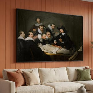 May include: Large framed print of Rembrandt's "The Anatomy Lesson of Dr. Nicolaes Tulp." The painting depicts a group of men gathered around a cadaver, with one man performing an anatomy demonstration. The artwork is displayed above a cream-colored sofa with decorative pillows.