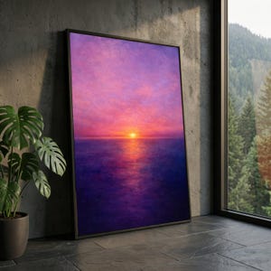 May include: Framed art print showing a sunset over the sea. The artwork displays a gradient of colours, with a bright orange sun setting over a deep purple sea. The sky transitions from pink to purple. The framed print is leaning against a concrete wall.