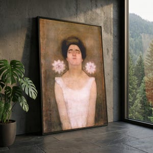 Könnte beinhalten: Gerahmter Kunstdruck mit einem Porträt einer Frau mit geschlossenen Augen und zwei rosa Blumen. Die Frau trägt ein weißes Kleid. Das Kunstwerk hat eine Vintage-Ästhetik mit einem dunklen Rahmen und wird vor einer grauen Wand ausgestellt.