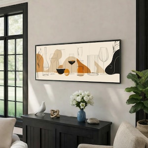 Può includere: Una stampa incorniciata raffigurante un disegno a tratto minimalista di calici e bottiglie di vino, con forme astratte in nero, arancione e beige. L'opera d'arte è presentata in una cornice nera, che esalta l'estetica moderna della stanza.