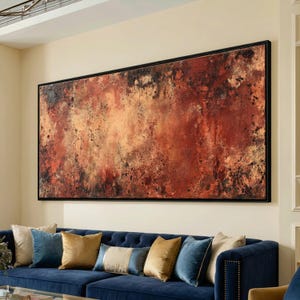May include: Large abstract painting with a textured surface in shades of red, brown, and gold, framed in black. The artwork hangs above a blue velvet sofa with various throw pillows.