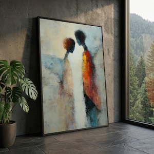 Könnte beinhalten: Abstraktes Gemälde in einem schwarzen Rahmen. Das Kunstwerk zeigt zwei Figuren mit verschwommenen Merkmalen, dargestellt in Orange-, Rot-, Blau- und Weißtönen. Das Gemälde lehnt an einer grauen Betonwand, mit einer Topfpflanze und einem Fenster im Hintergrund.