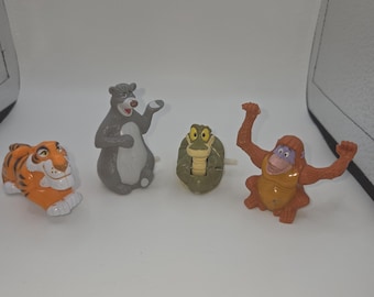 May include: A set of four plastic animal figurines including an orange and black striped tiger, a grey bear with a white belly, a green coiled snake with yellow eyes, and a brown orangutan with arms raised, all standing in a horizontal row.