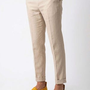 May include: Tan linen pants with a cuffed hem paired with yellow leather slip-on shoes. The shoes have a multi-colored striped sole. The pants have a classic, tailored fit.