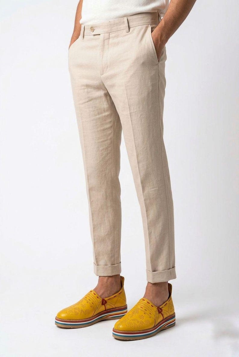 May include: Tan linen pants with a cuffed hem paired with yellow leather slip-on shoes. The shoes have a multi-colored striped sole. The pants have a classic, tailored fit.
