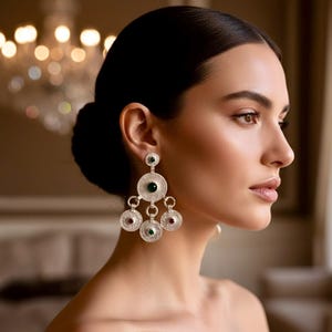 Peut inclure: Boucles d'oreilles pendantes argentées avec un design circulaire, ornées de pierres précieuses vertes et rouges. Les boucles d'oreilles présentent un motif détaillé et texturé et sont suspendues à un petit clou. Le design est élégant et accrocheur.