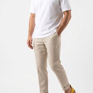May include: A person wearing a white t-shirt, beige linen pants, and yellow leather loafers. The pants are cuffed at the ankles. The loafers have a multi-colored sole. The outfit is casual and stylish.