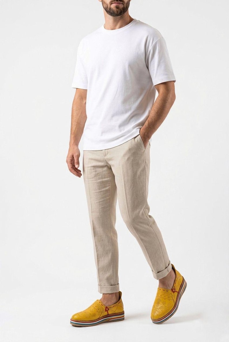 May include: A person wearing a white t-shirt, beige linen pants, and yellow leather loafers. The pants are cuffed at the ankles. The loafers have a multi-colored sole. The outfit is casual and stylish.