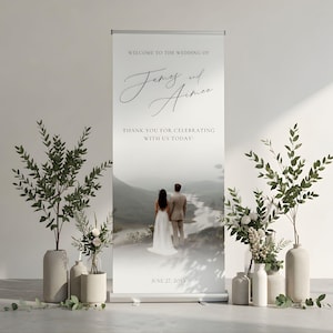 Peut inclure: Une bannière de bienvenue de mariage avec les noms "James et Aimee" en écriture élégante. La bannière présente une photo panoramique d'un couple surplombant un paysage. Le texte "MERCI DE CÉLÉBRER AVEC NOUS AUJOURD'HUI !" et la date "27 JUIN 20XX" sont également affichés.