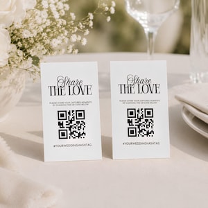 Pode incluir: Dois cartões retangulares brancos com o texto preto Share THE LOVE, seguido pela instrução Please share your captured moments by scanning the QR code below, um código QR em preto e branco e a hashtag #YOURWEDDINGHASHTAG.
