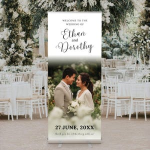 Peut inclure: Panneau de bienvenue de mariage avec les noms "Ethan et Dorothy" en écriture cursive. Le panneau affiche une photo du couple et la date "27 JUIN, 20XX". L'arrière-plan montre une réception de mariage avec des tables et des décorations florales.