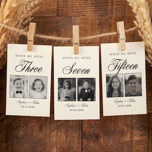 May include: Three cards with black and white photos of children are clipped to a string with wooden pegs. The cards read "When We Were" and feature the ages "Three," "Seven," and "Fifteen." The names "Sophia + Allen" and a date are printed below each photo.