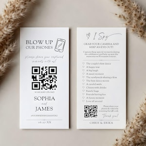 May include: Two white wedding cards with black text and illustrations. One card reads "Blow Up Our Phones" with a phone graphic and QR code. The other card says "I Spy" with a list of wedding moments and a QR code.