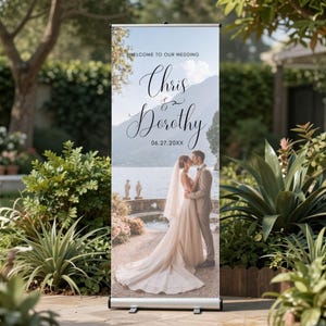 May include: A wedding welcome banner with the names "Chris & Dorothy" and the date "06.27.20XX" in elegant script. The banner features a photo of a couple kissing, with a scenic background of a lake and mountains.