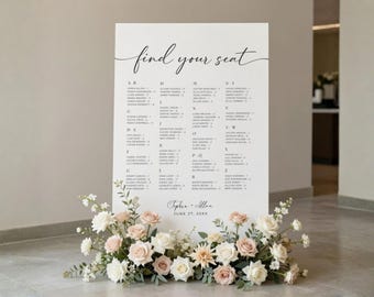 May include: A large white wedding seating chart with elegant calligraphy that reads "find your seat." The chart lists names alphabetically. A floral arrangement of white and blush roses and greenery sits at the base. The date is June 27, 20XX.
