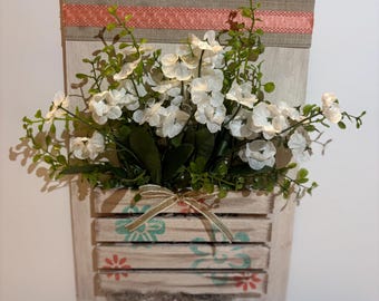 バスケットと造花の白い花と緑の植物が飾られた素朴な木製の壁掛け