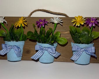 手作りの造花が入った3つの小さな青い鉢が飾られた壁掛け