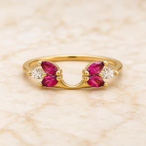 May include: A gold ring featuring a curved band design adorned with four marquise-cut vibrant pink stones and two smaller marquise-cut clear white stones, arranged in two symmetrical clusters on either side of the center opening.