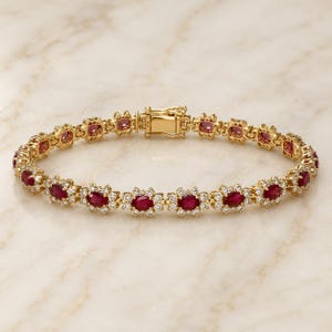 May include: A gold link bracelet featuring a series of oval-cut deep red rubies, each surrounded by a halo of small clear white diamonds. The bracelet is connected by a secure gold box clasp mechanism, creating a continuous circular design.