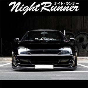 Puede incluir: Un coche deportivo negro con el texto "Night Runner" en escritura blanca en la parte superior y en el parabrisas. El coche está estacionado sobre una superficie gris, con un fondo oscuro. El coche tiene un perfil bajo y un alerón delantero.