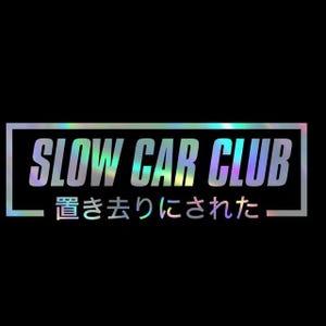 May include: A holographic sticker featuring the text "SLOW CAR CLUB" in capital letters, with Japanese characters underneath. The text is enclosed in a white rectangular frame on a black backdrop.