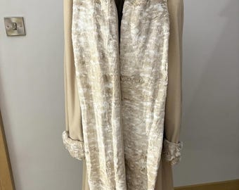 May include: A beige coat with a faux fur scarf draped over it. The scarf is a mix of light and dark beige, creating a textured appearance. The coat has matching fur trim on the cuffs.