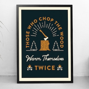 May include: A framed print with a dark blue background and white text that reads "Those who chop the wood warm themselves twice". The text is surrounded by a stylized sunburst design with an axe sticking into a tree stump. There are two small trees on either side of the stump.