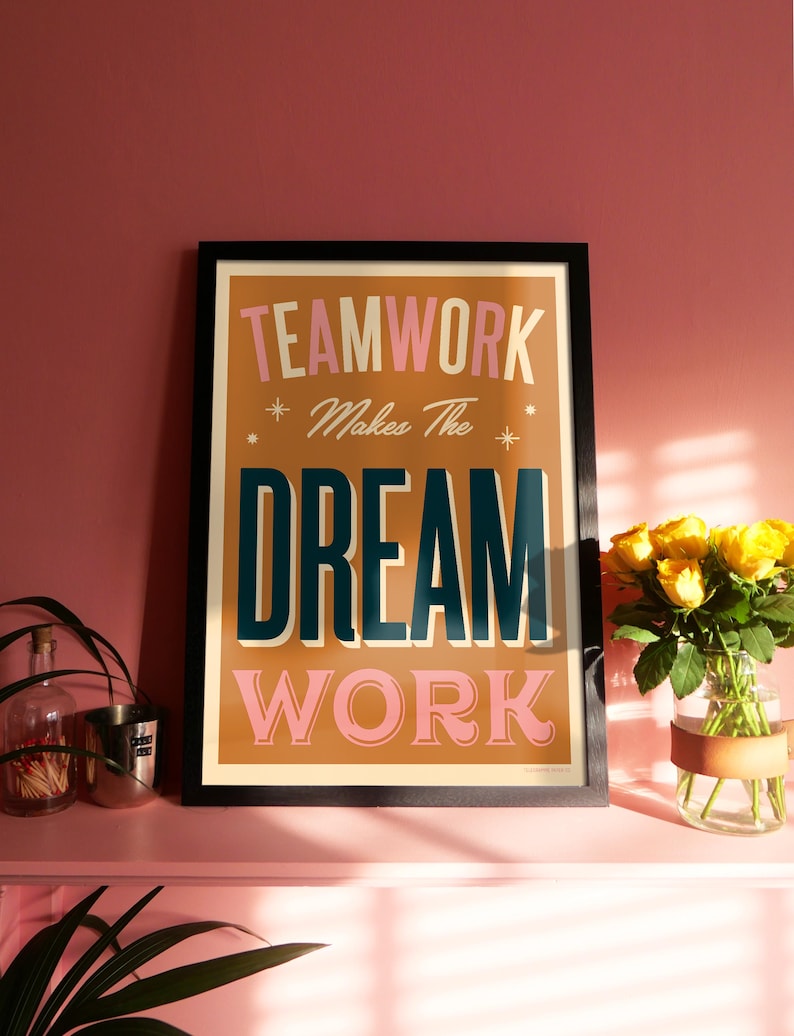 May include: A framed motivational poster with the text "TEAMWORK Makes The DREAM WORK" in a retro style with pink, orange, and blue lettering on a brown background.