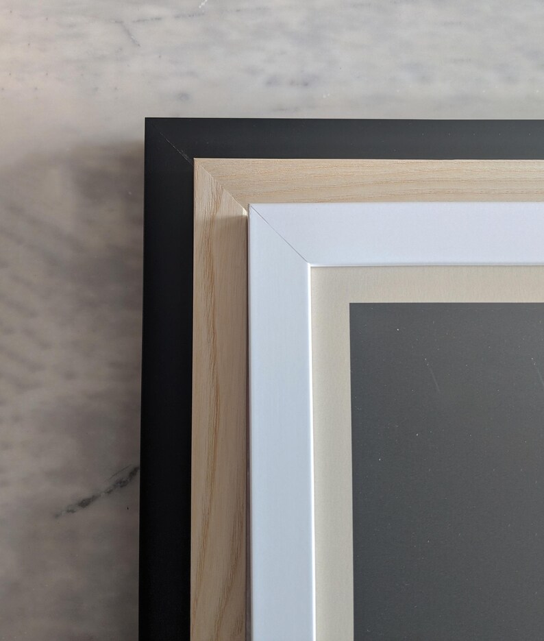 May include: Close-up of the corner of a picture frame with three layers of framing. The outer frame is black, the middle frame is natural wood, and the inner frame is white.