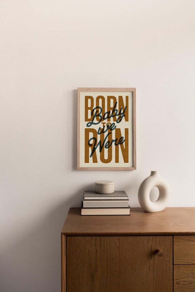 May include: A framed print with a beige background and brown text that reads "Born to Run" with the words "Baby we" in black cursive script.