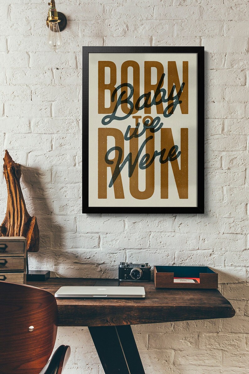 May include: A framed print with a white background and black frame. The print features the text "Born to Run" in a brown font with the word "Baby" in a blue font.