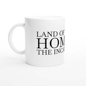 Op de afbeelding: Witte keramische mok met een gebogen handvat. De mok heeft de zwarte tekst "LAND OF HOME THE INCA" in het midden op de voorkant. De mok is ontworpen voor warme dranken.