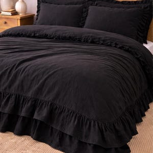 Puede incluir: Juego de cama negro con dos fundas de almohada a juego. La colcha y las fundas de almohada tienen un aspecto suave y texturizado. La cama está colocada contra un cabecero tejido y una alfombra de color neutro.