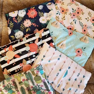 May include: A collection of fabric pouches with various floral, cactus, and geometric patterns. The pouches feature a range of colors, including navy, pink, black, and teal. The fabrics are arranged on a brown, textured surface.