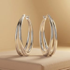 May include: A pair of silver hoop earrings featuring a double-layered design. Each earring consists of two interconnected smooth, polished silver bands that form a continuous oval shape. The metal is stamped with S925, indicating sterling silver.