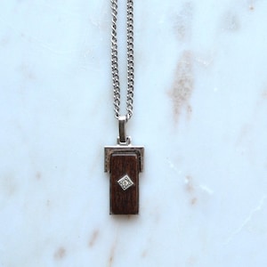 May include: Silver-tone necklace with a rectangular pendant. The pendant features a dark brown wooden inlay and a small, square-shaped diamond. The necklace hangs on a silver chain.