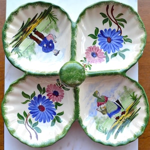 May include: A decorative, four-section serving dish with a green trim and a central green knob. Each section features a hand-painted scene with flowers and figures in a whimsical style. The dish is white with green trim.