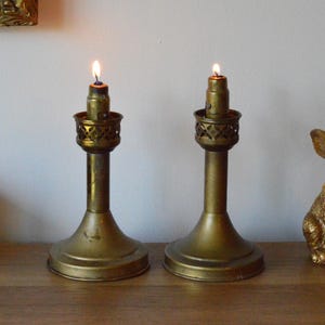 May include: Two antique brass candle holders with lit candles and a gold bunny figurine. The candle holders have a decorative openwork design and are placed on a wooden surface. The bunny is sitting upright.