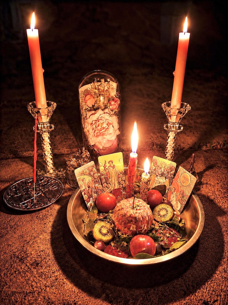 May include: A mystical arrangement featuring lit candles, tarot cards, and a bowl of fruit. Two tall candles flank a central display with a glass dome containing flowers. The scene is illuminated with warm light, creating a spiritual ambiance.