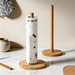 Peut inclure: Un porte-essuie-tout en bambou avec un rouleau d'essuie-tout blanc décoré de cœurs verts et de graphiques noirs. Le support a une base ronde et une cheville en bois. Un deuxième support en bambou est également visible.