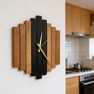 Könnte beinhalten: Eine moderne Wanduhr mit geometrischem Design. Sie besteht aus vertikalen Holzplanken in Naturholz und Schwarz. Goldfarbene Zeiger zeigen die Uhrzeit an. Die Uhr ist an einer weißen Wand befestigt.