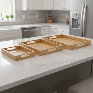 May include: Three rectangular bamboo serving trays of varying sizes with cut-out handles. The trays are light brown and sit on a white countertop in a kitchen setting. The largest tray is approximately 46 cm long.