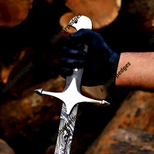 Pode incluir: Uma espada com uma l&acirc;mina de a&ccedil;o de Damasco estampada e uma guarda de cor prateada polida. O cabo &eacute; escuro com um pomo arredondado. O texto Adisharpedges &eacute; vis&iacute;vel v&aacute;rias vezes na imagem, sobrepondo-se &agrave; l&acirc;mina e ao cabo da espada.