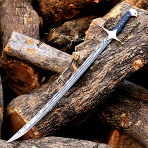 Pode incluir: Uma espada com uma l&acirc;mina longa e curva de a&ccedil;o de Damasco com um padr&atilde;o ondulado distinto. O punho &eacute; azul-escuro com tr&ecirc;s rebites prateados, um pomo prateado e uma guarda em cruz prateada com extremidades pontiagudas.