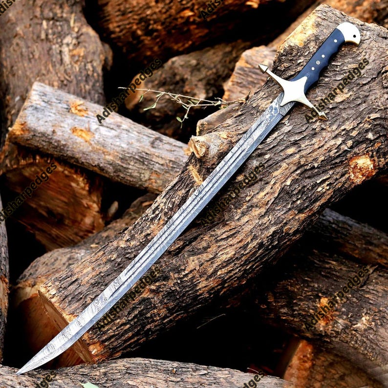 Pode incluir: Uma espada com uma l&acirc;mina longa e curva de a&ccedil;o de Damasco com um padr&atilde;o ondulado distinto. O punho &eacute; azul-escuro com tr&ecirc;s rebites prateados, um pomo prateado e uma guarda em cruz prateada com extremidades pontiagudas.