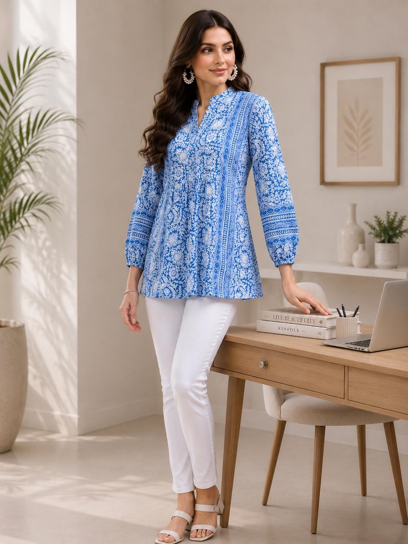 May include: A long-sleeved tunic top featuring a vibrant blue and white floral pattern with a split neckline and gathered cuffs, paired with slim-fit white trousers and light-colored open-toe sandals, creating a coordinated ensemble.