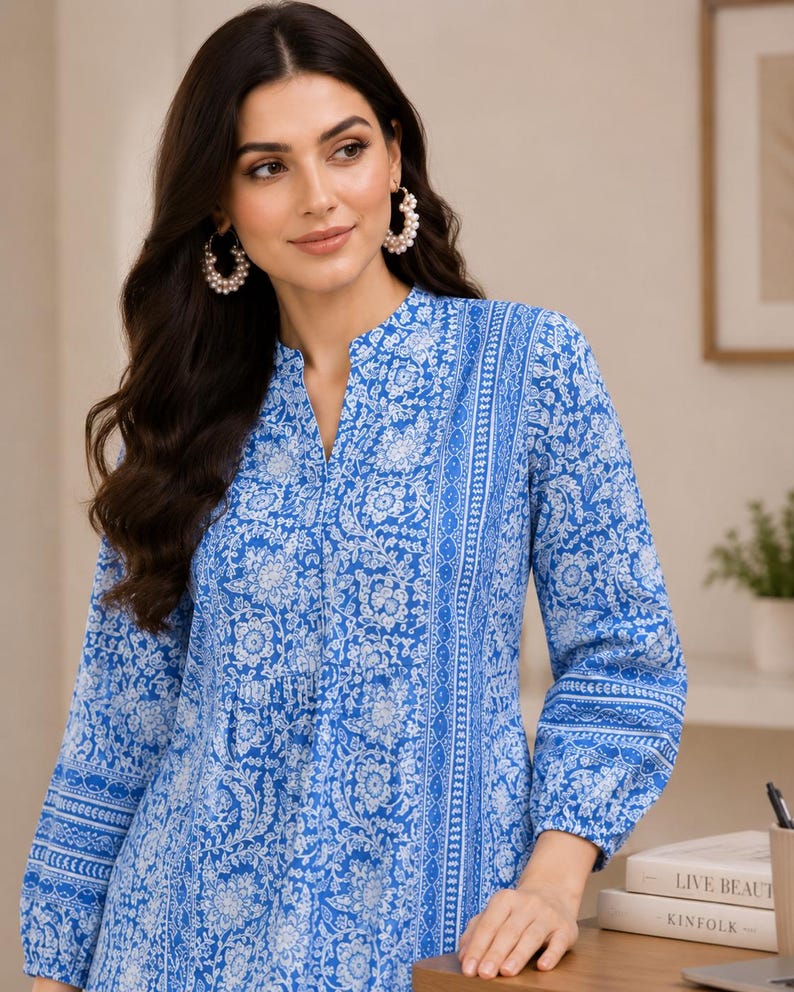May include: A long-sleeved tunic featuring a vibrant blue and white floral pattern with a split neckline. The garment displays intricate botanical motifs and vertical striped borders along the front and sleeves, finished with gathered cuffs at the wrists.