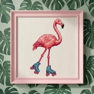 May include: Cross-stitch art of a pink flamingo wearing blue roller skates, framed in a pink square frame. The flamingo is set against a cream-colored background. The background wallpaper has a green tropical leaf pattern.